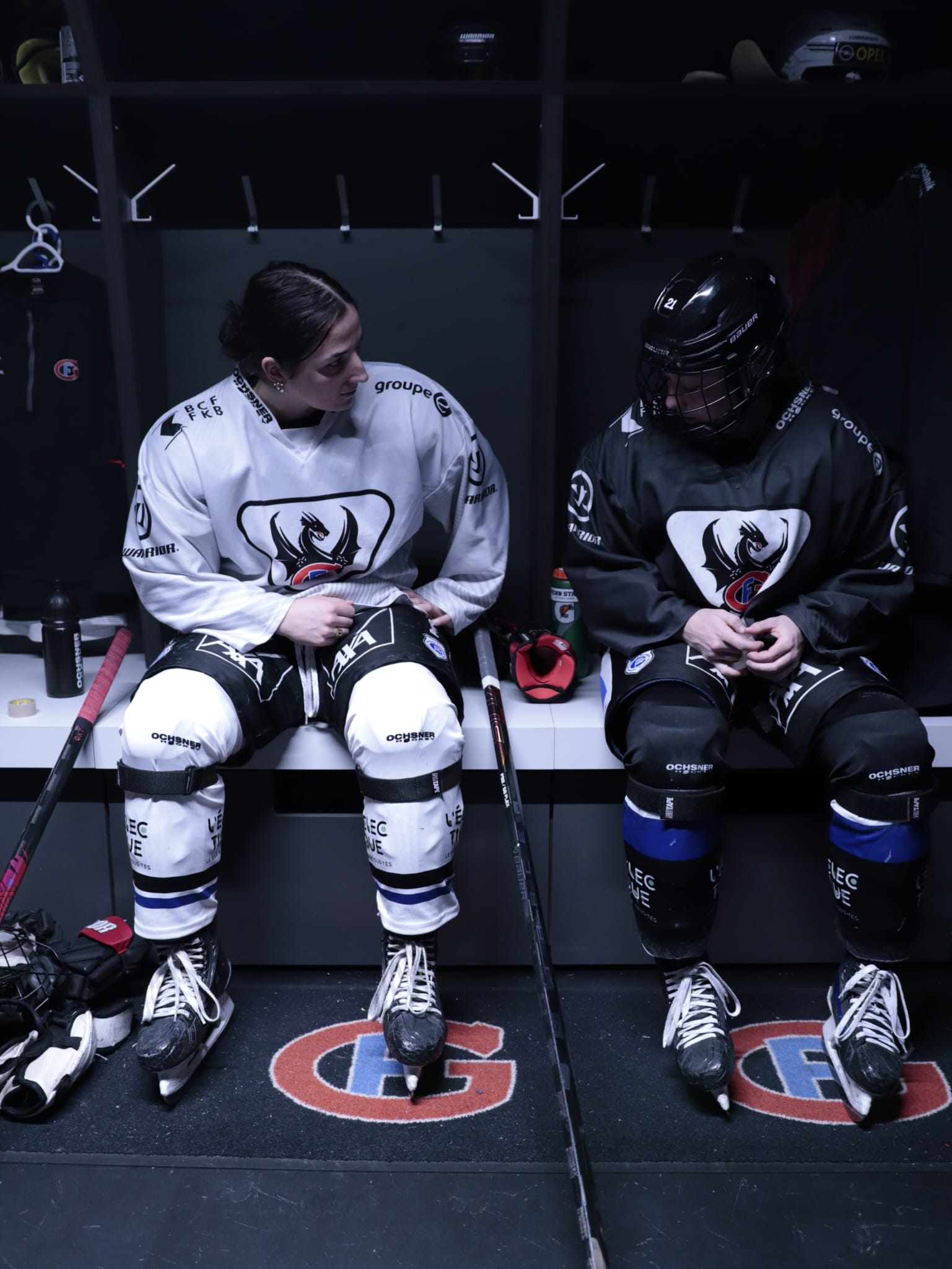 Two women ice hockey players with NOTAPE bands on shin guards instead of single used tape in the locker room